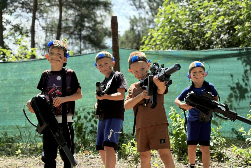Uśmiechnięte dzieci stojące z karabinami paintballa laserowego